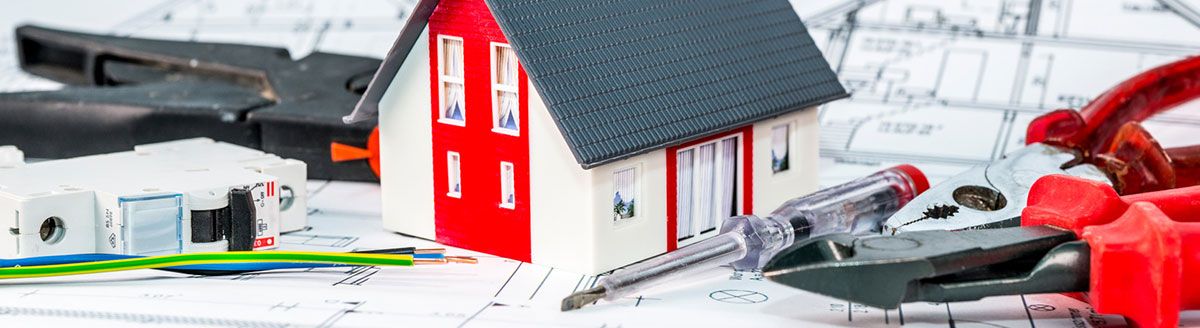 Hausmodell mit Werkzeug und Sicherungsautomat auf einem Bauplan
